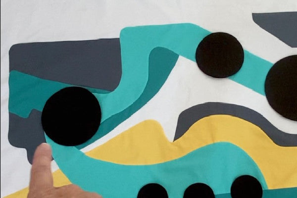 Appliqued quilt top in teal, yellow and charcoal with black circles laid over curved shapes