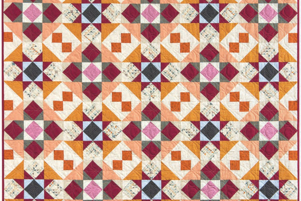 Foundry quilt in warm coral, amber, magenta and ivory, thirty blocks of small squares set on point that read as diamonds and pinwheels across the surface