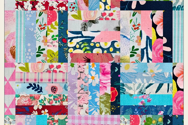 Garden Fence baby quilt in pink, blue, teal and navy floral and gingham prints, twelve rail fence blocks turned a quarter turn from each other inside a scrappy pieced border