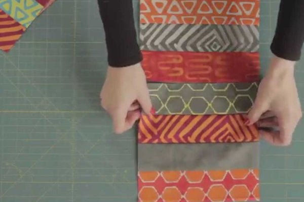 Jelly roll strips sewn into a coin quilt row on a cutting mat, the layout Mary Fons calls the easiest quilt ever