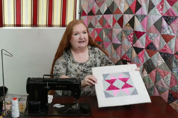 a Keyhole Star quilt block in pink and gray, made from four half square triangles and two flying geese