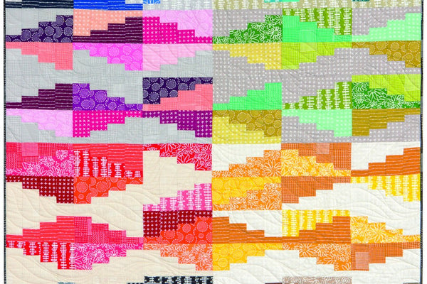 Prismatic Echoes quilt with eight color blocks, blue, teal, purple and pink, green, red, orange and yellow, gray and brown, each built from stepped rectangles rising and falling against cream and gray backgrounds