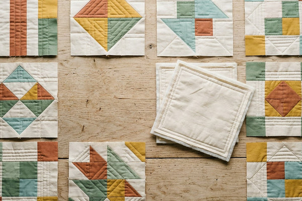 Finished quilt as you go blocks laid out on a wooden table, each block already quilted, with two blocks turned over to show their own backing and batting