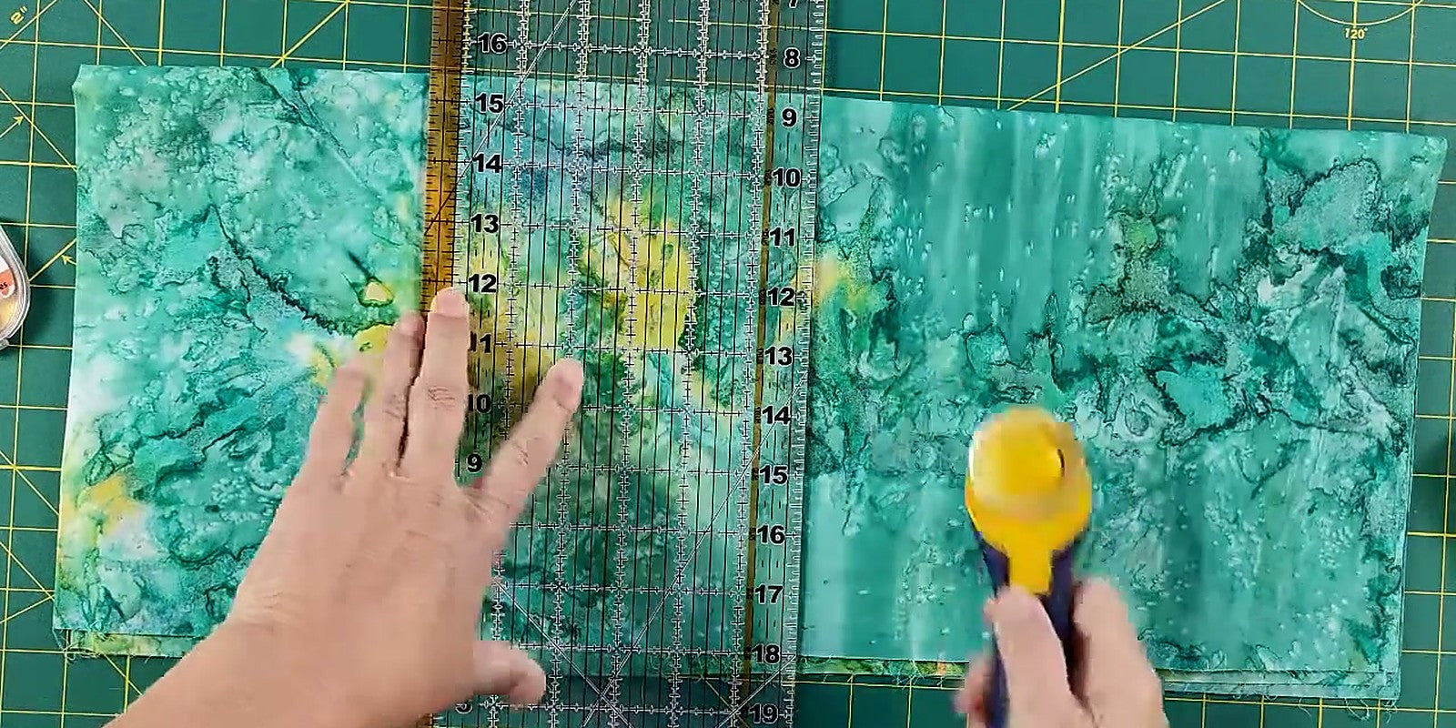 Rotary cutter halfway through a cut along an acrylic ruler held flat on batik cotton - The Fabric Hut