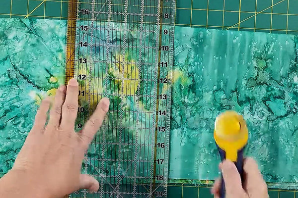 Rotary cutter halfway through a cut along an acrylic ruler held flat on batik cotton - The Fabric Hut