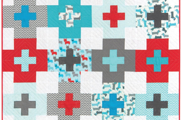 The Plus Side quilt, twenty plus blocks in red, teal, aqua, charcoal, gray chevron and dog prints on a white background, each large plus holding a smaller plus of a second fabric, bound in red