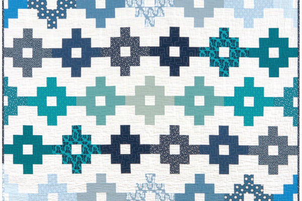 The Woven quilt by Elizabeth Hartman, rows of navy, teal, blue and gray crosses on a white background, each cross open at the center and linked to the next by a full width bar, with the rows offset by half a block